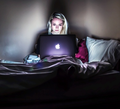 woman sitting with MacBook in dark on bed