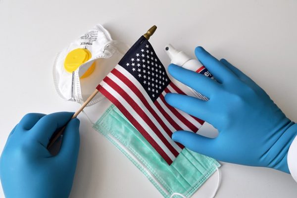 American flag with PPE and gloved hands on white backdrop