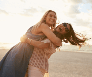 two women holding each other on the beach while laughing at sunset