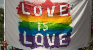 White flag painted with LGBTQIA+ rainbow with words "love is love"