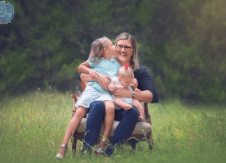 mother hugging 2 daughters on a chair in a field