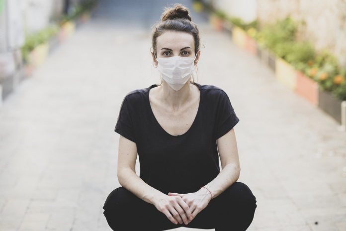 woman sitting on the ground and wearing a protective mask