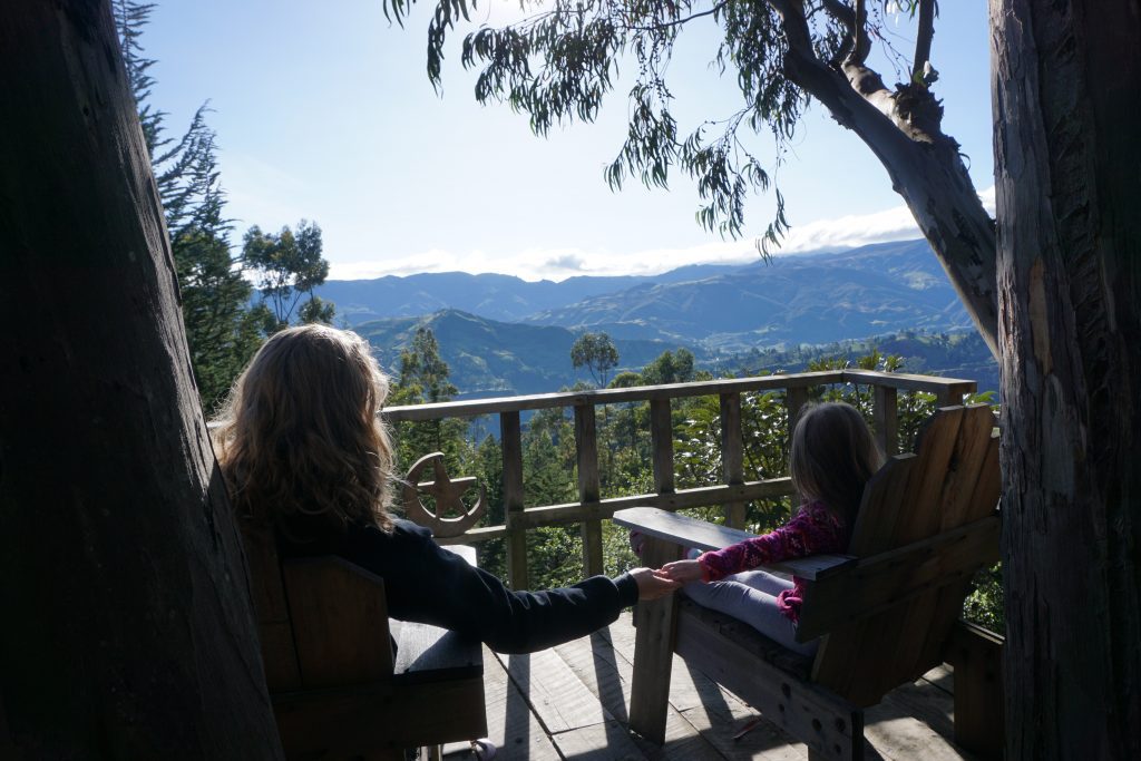 mom holding little girl's hand in porch chairs on a deck overlooking mountains