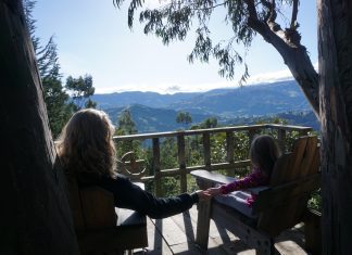 mom holding little girl's hand in porch chairs on a deck overlooking mountains
