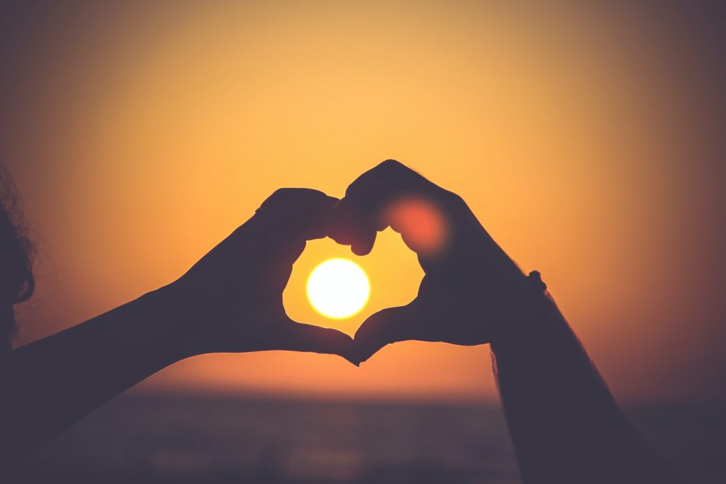hands making a heart against a setting sun