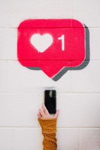 A hand reaches for a mobile phone. A red box with a white heart and a number one is above the phone. 