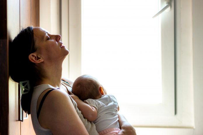 Woman holding infant appearing tired, concerned, sad, depressed