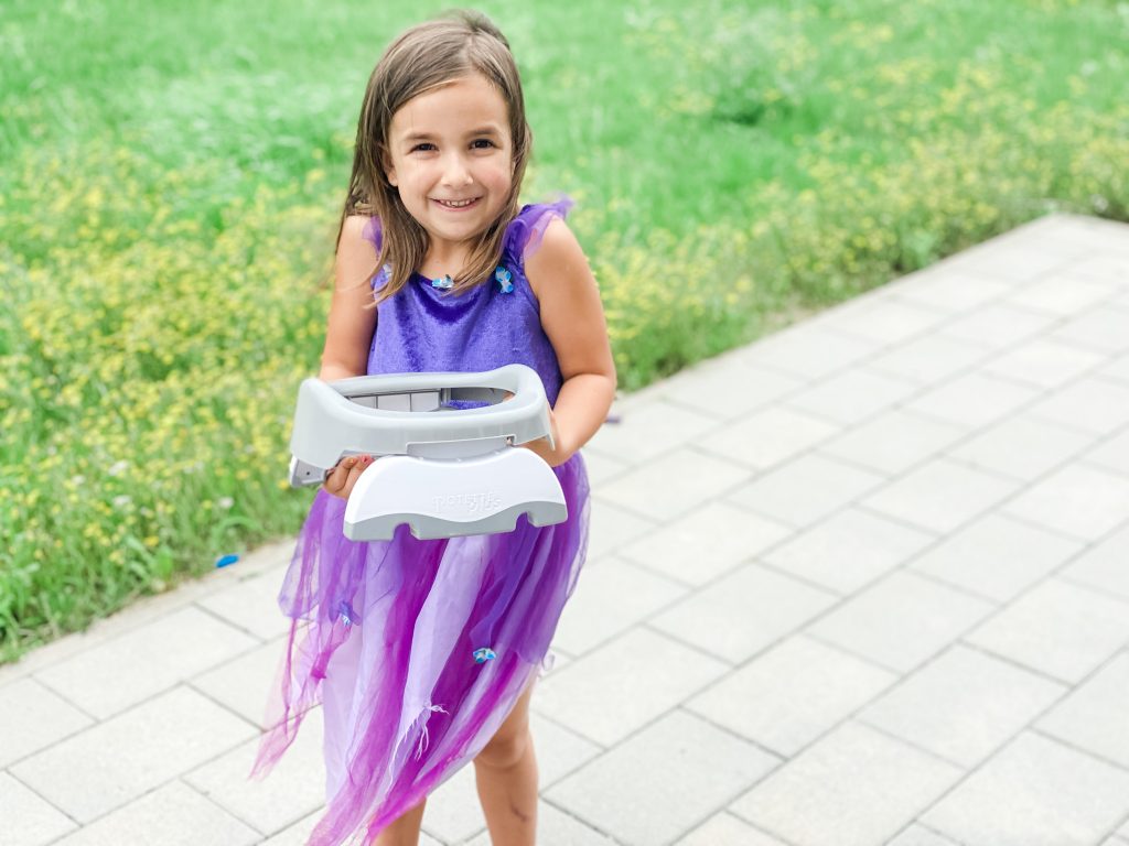 young girl in a purple dress holding a travel or portable potty seat