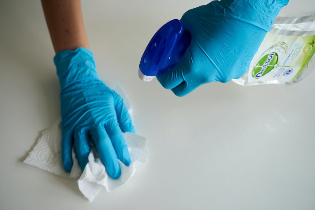 person wearing gloves cleaning a countertops with spray and towel