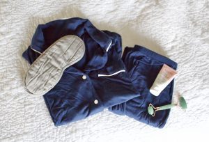Navy pajamas on a white bed with a sleep mask, jade roller, and facial cream (three Friday Favorites)