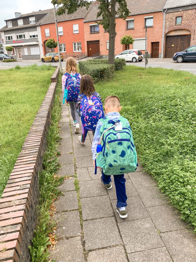 three elementary aged kids walking with backpacks on a brick path