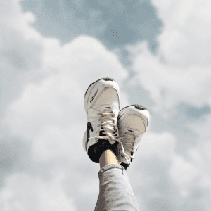 white running shoes and legs up in the air with cloud background