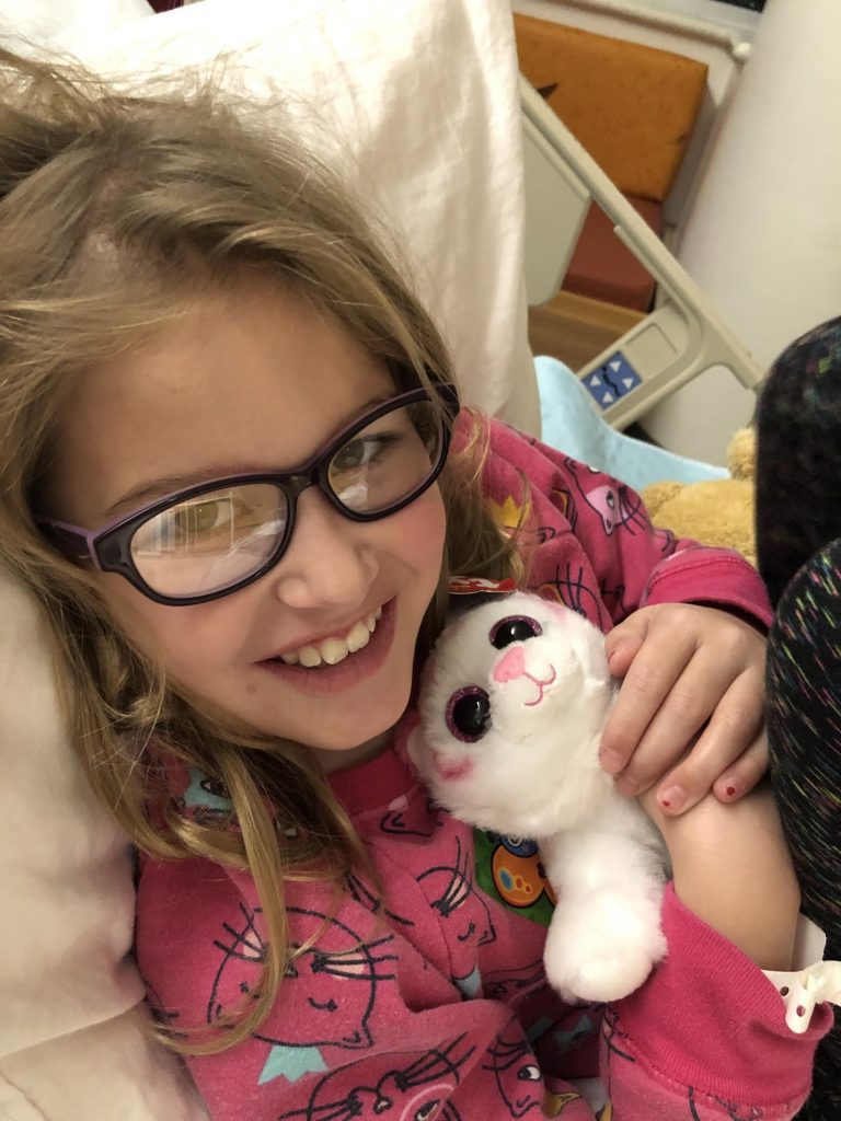 girl smiling in hospital bed holding a stuffed animal