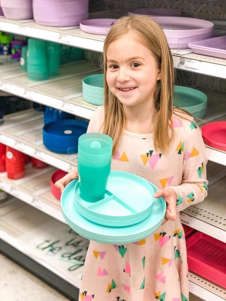 young girl holding a set of colored dishwater in a store