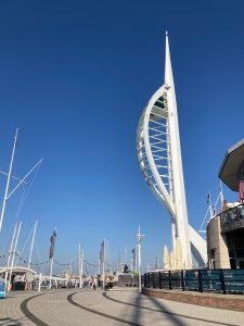 The Spinnaker Tower can be seen outlined against a clear, blue sky. the tower has a straight edge on the right with a curved edge on the left.
