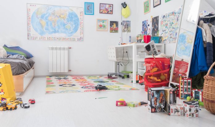 children's room with posters and map on the wall, toys cluttered on the floor and dresser, and a messy bed