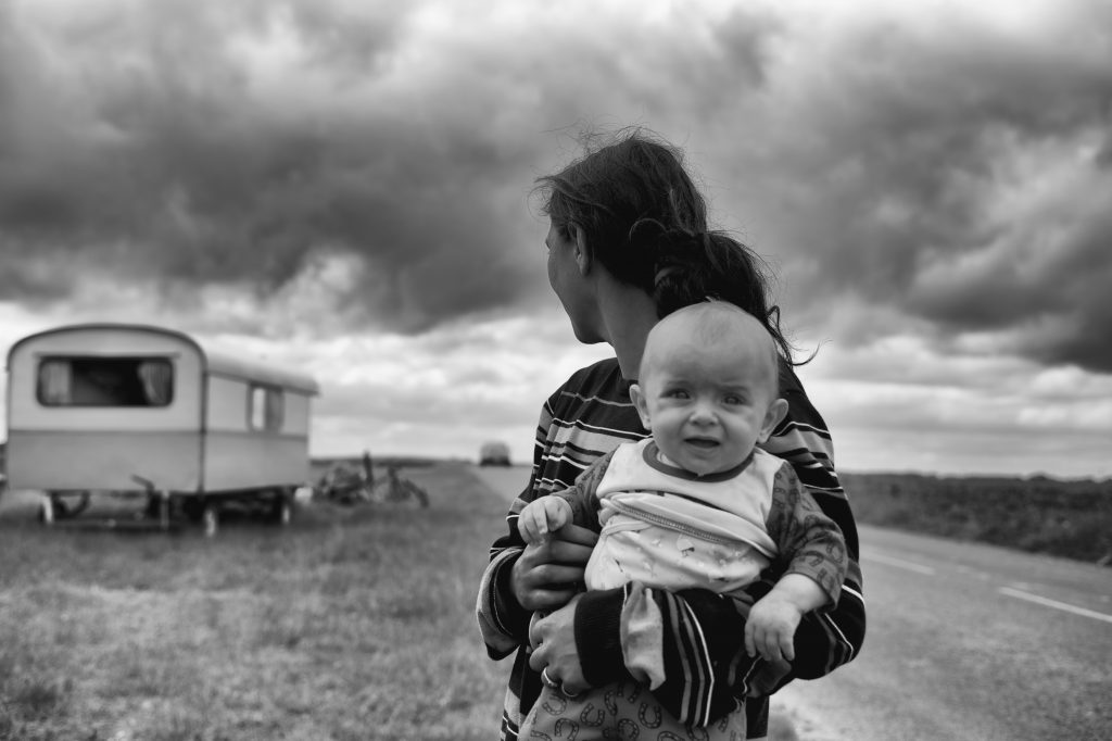 parent holding a child in a dry land with a trailer in the background, black and white photo
