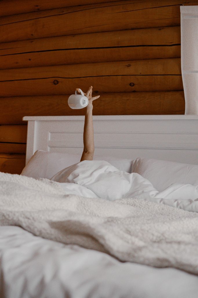 woman's arm reaching up from bed holding coffee cup