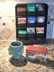 tea packets in a holder with a Buddha mug and cinnamon apple spice tea on a kitchen counter