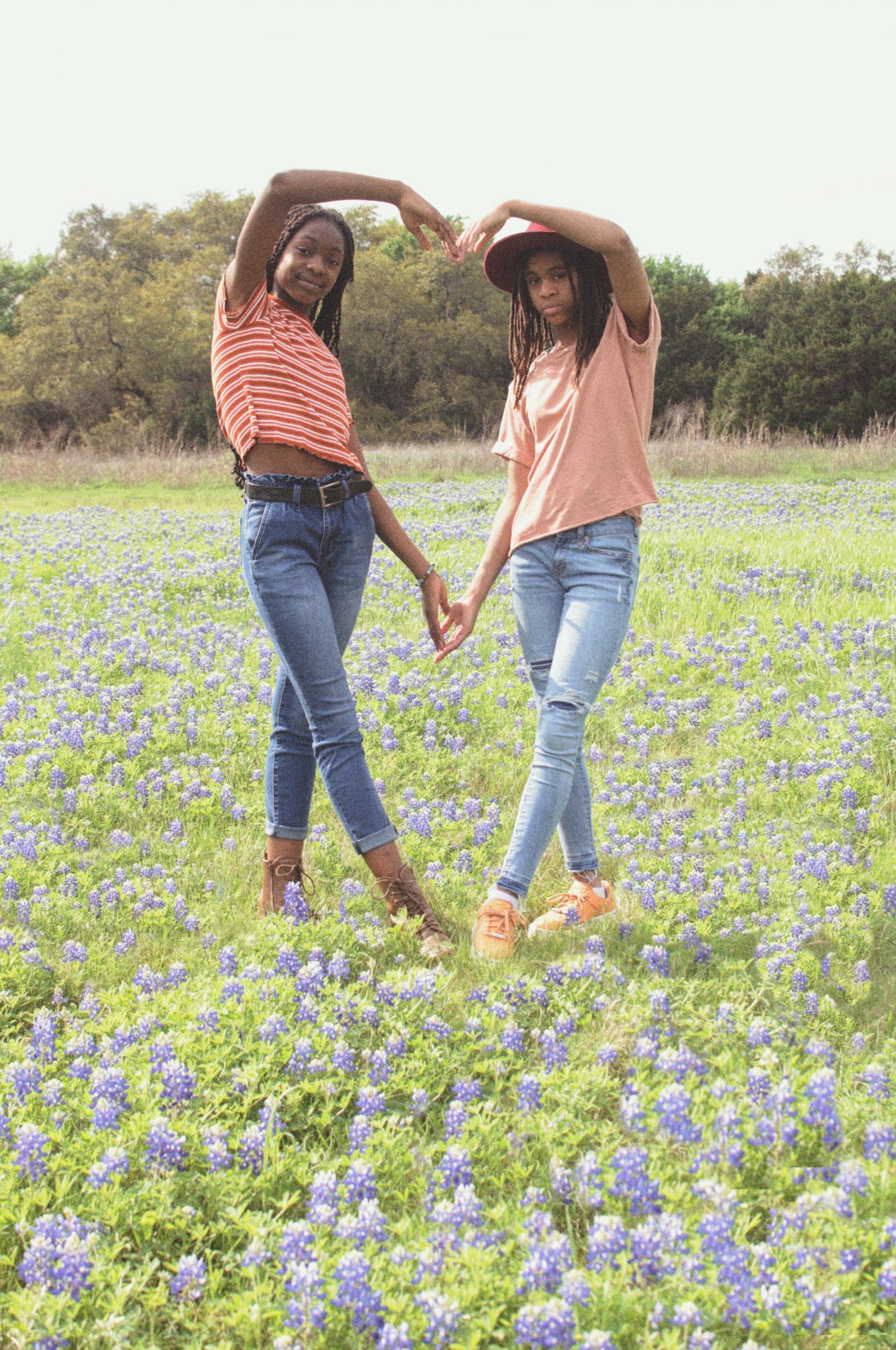 two teens girls standing in a field of flowers making a heart with their arms
