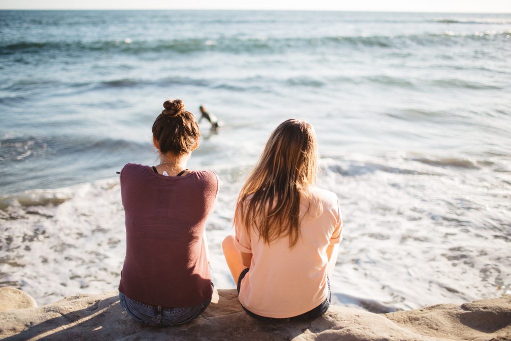 two women sitting on the beach and staring out at the ocean