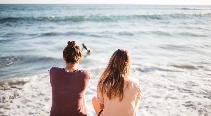 two women sitting on the beach and staring out at the ocean