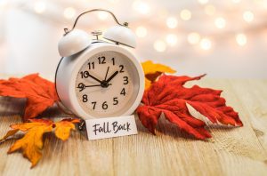 White clock sits on orange, red, and yellow leaves with a card that says "fall back"