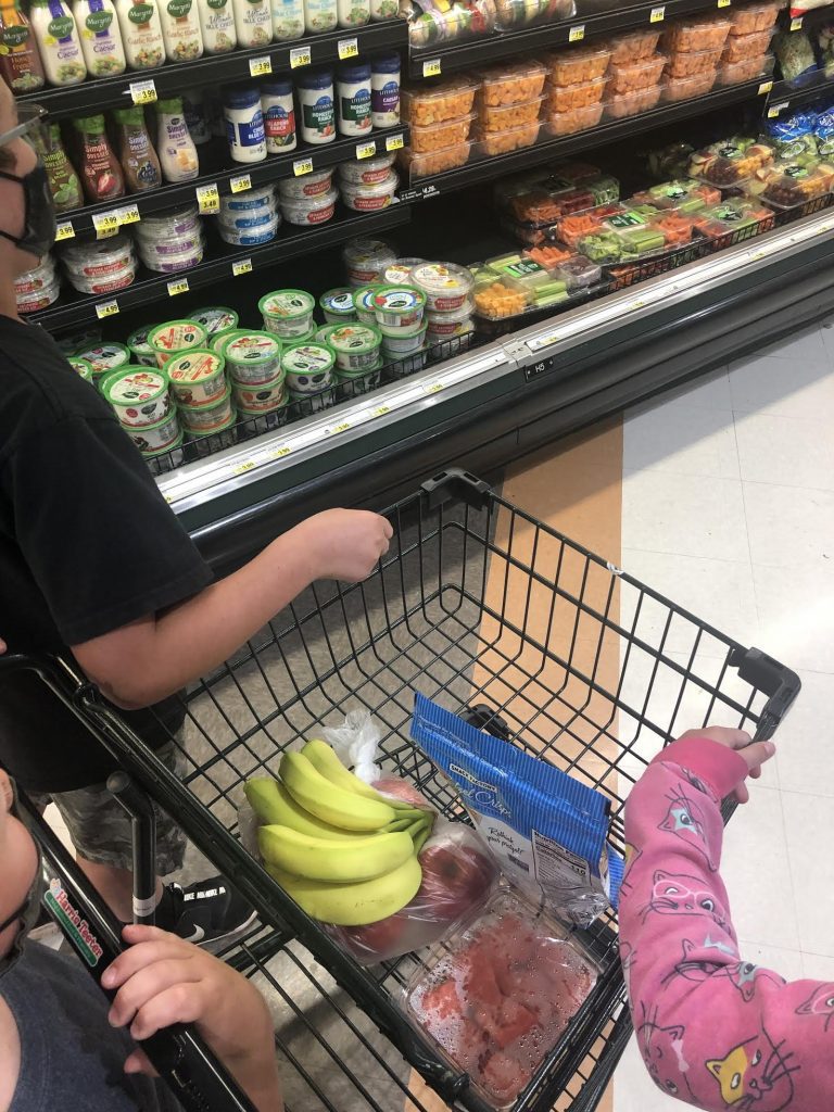 shopping cart with groceries and children's hands holding onto the edge of the cart