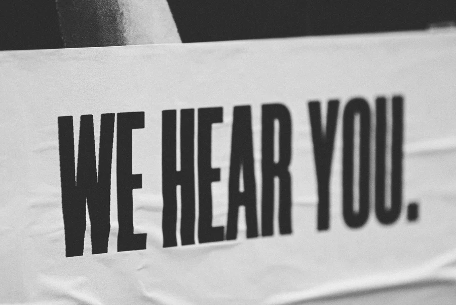 white poster with "WE HEAR YOU" in black text