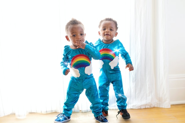 twin boys in blue onesies with rainbows on them standing in the sunlight