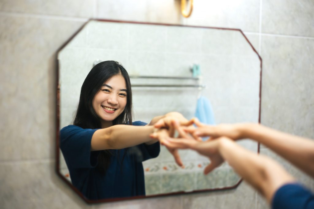 Young adult Asian woman practices positive self-talk in the mirror