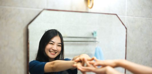 Young adult Asian woman practices positive self-talk in the mirror