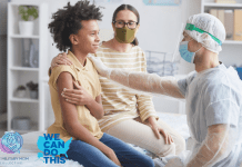 son with mother at a doctor's office holding a piece of gauze to his arm while a physician in PPE rests a hand on his shoulder, signaling comfort. We Can Do This and MMC logos in the bottom left corner