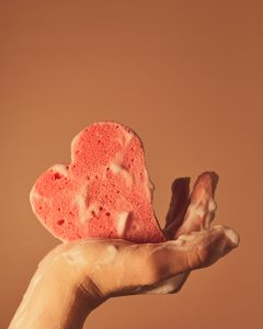 person holdng up a heart-shaped pink sponge with soap