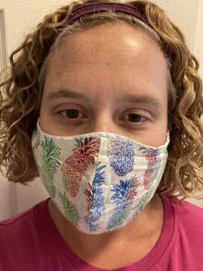 Woman with short, curly hair is wearing a colourful face mask.