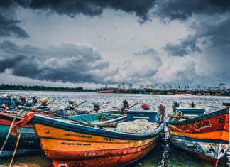 Wooden boats can be seen in the foreground with storm clouds in the sky behind them.