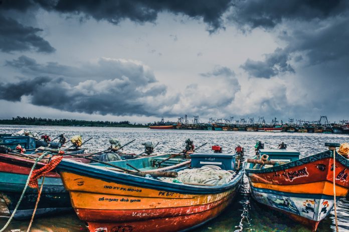 Wooden boats can be seen in the foreground with storm clouds in the sky behind them.