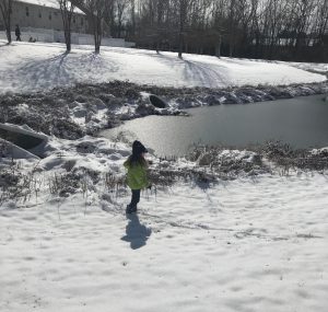 child standing outside in the snow near a frozen pond
