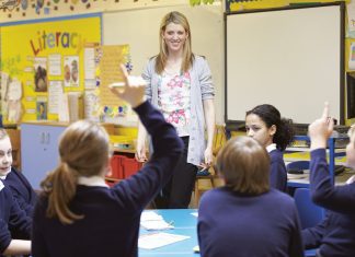 teacher standing in a classroom with students raising their hands
