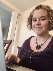 A white woman with short curly hair sits at a laptop, hand poised, ready to type.