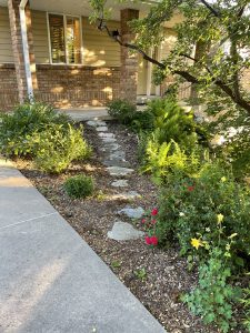 A rock path leading up to a cement porch with flowers to the left and right.