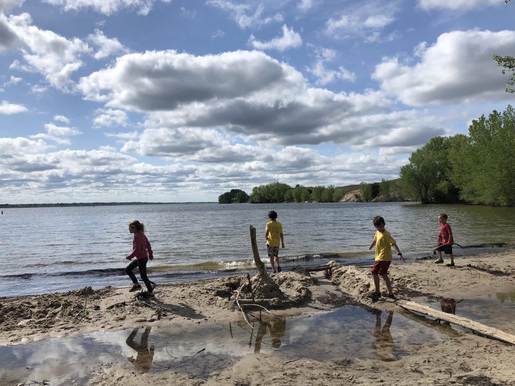 4 kids run across a beach at a lake