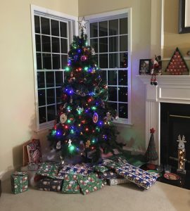 A christmas tree sits in the corner of a room. The lights on the tree are lit and presents are wrapped underneath the tree.