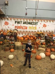 A girl stands in a pumpkin patch with hay bales and pumpkins around her.