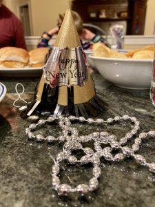 New Year's Hat sits on a table in front of party food. Silver beads are also on a chain in the foreground.