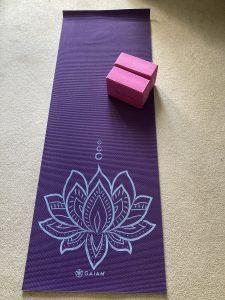 Purple yoga mat featuring a lotus flower lies on the floor. There are two pink yoga blocks on top of it.