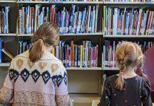 Two children read books in front of library shelves.