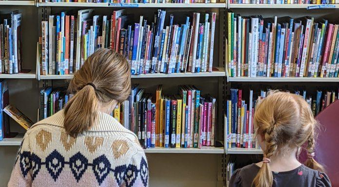 Two children read books in front of library shelves.