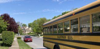 A yellow school bus is the main focus. It is pulling away on a residential street