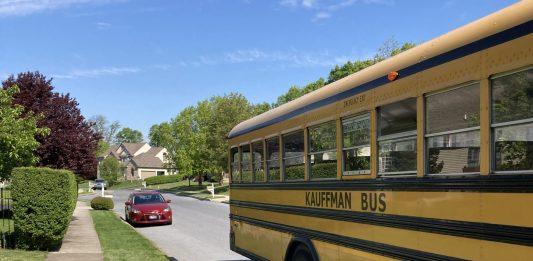 A yellow school bus is the main focus. It is pulling away on a residential street